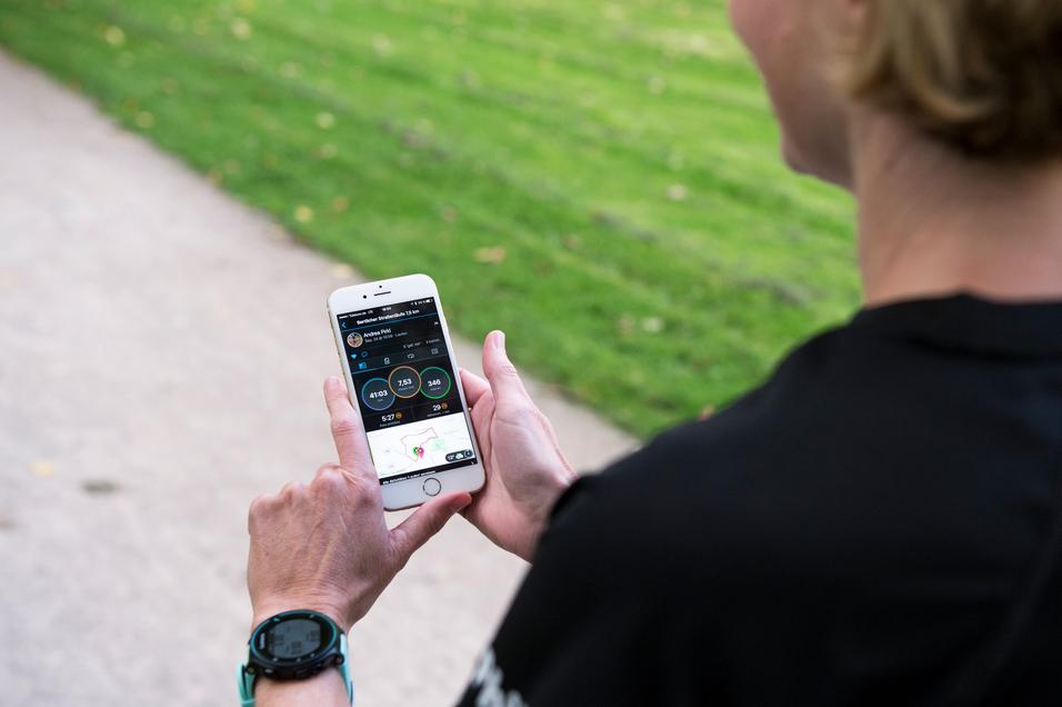 Person hält ein Smartphone mit Laufstatistiken in der Hand, während sie auf einem Weg im Freien steht.